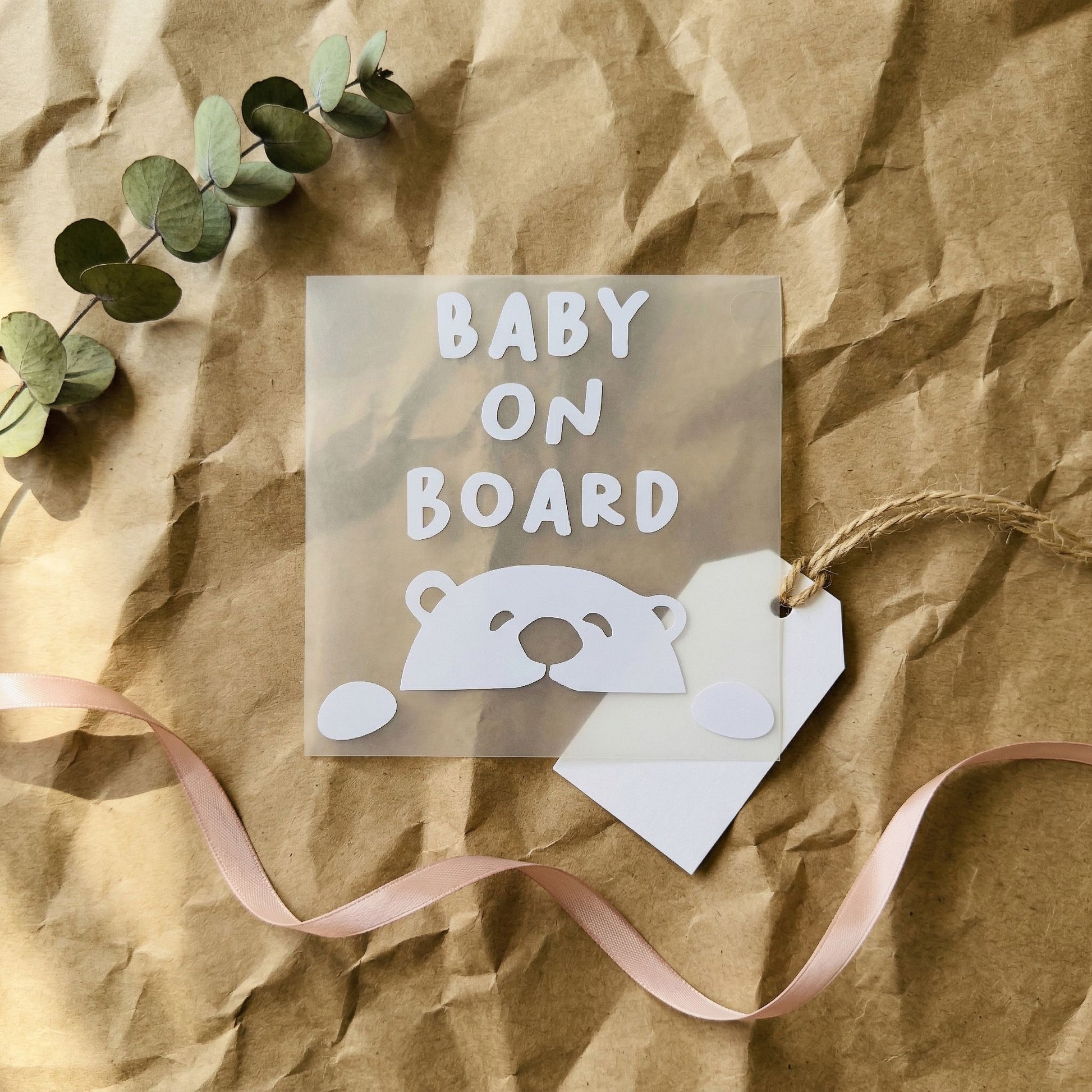 Baby on board sign with a bear illustration on crumpled brown paper with a pink ribbon.
